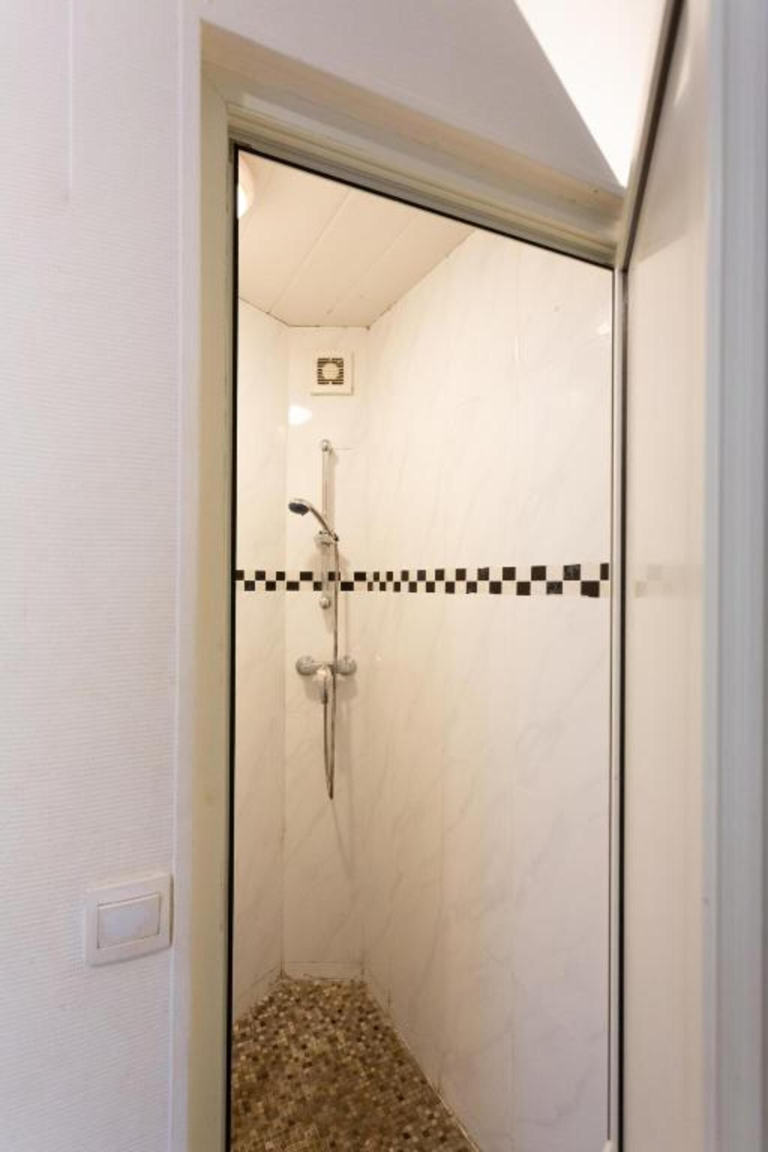 A glass-enclosed shower with a checkered tile border, a visible showerhead, and a control panel on the wall.