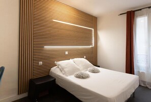 Une chambre à coucher moderne avec une tête de lit en lattes de bois, un lit blanc agrémenté d’oreillers moelleux et une table de chevet.