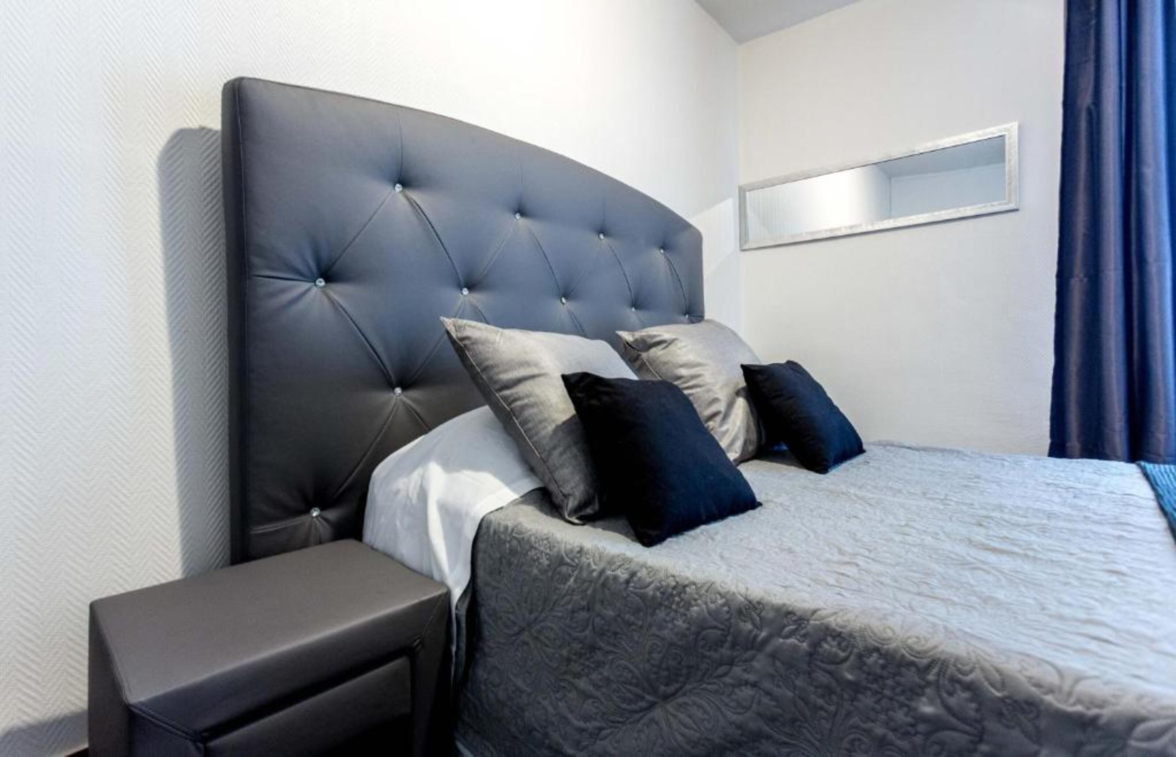 Une chambre à coucher moderne avec une tête de lit capitonnée, une couvre-lit grise et deux oreillers.
