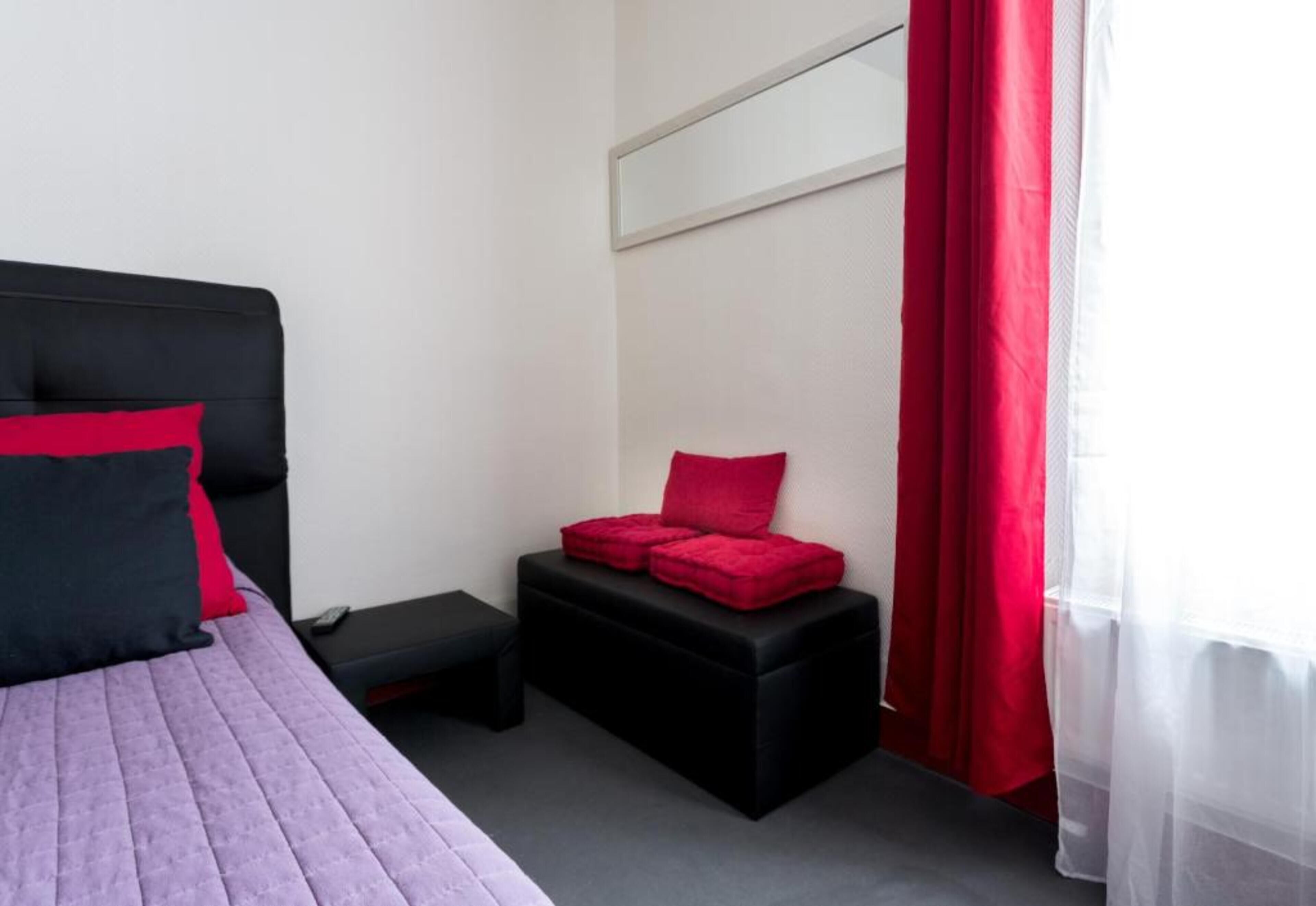 A bedroom with a bed, a small black bench, and a red cushion.