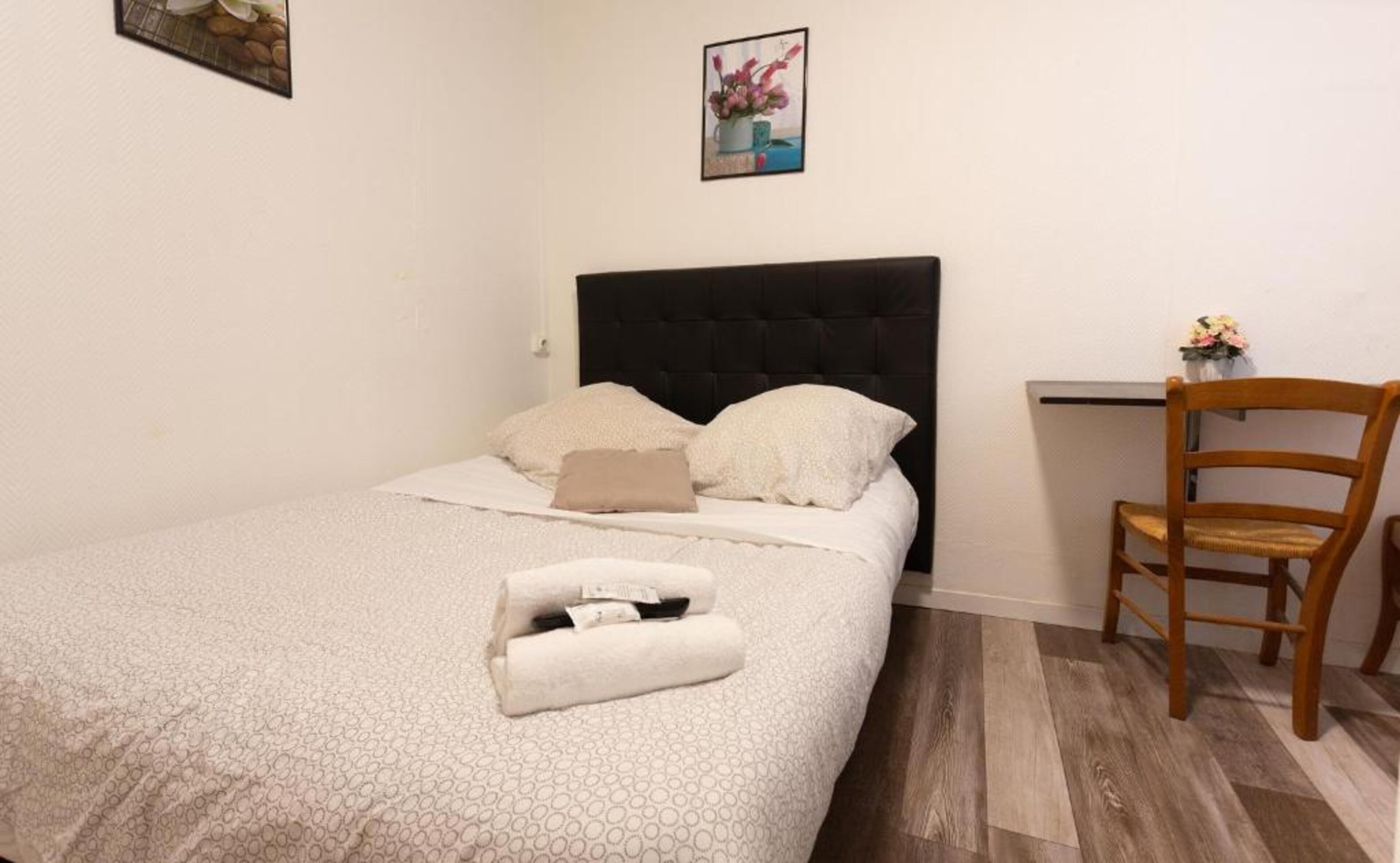 A neatly made bed with a patterned bedspread, two pillows, and a rolled towel on the side.