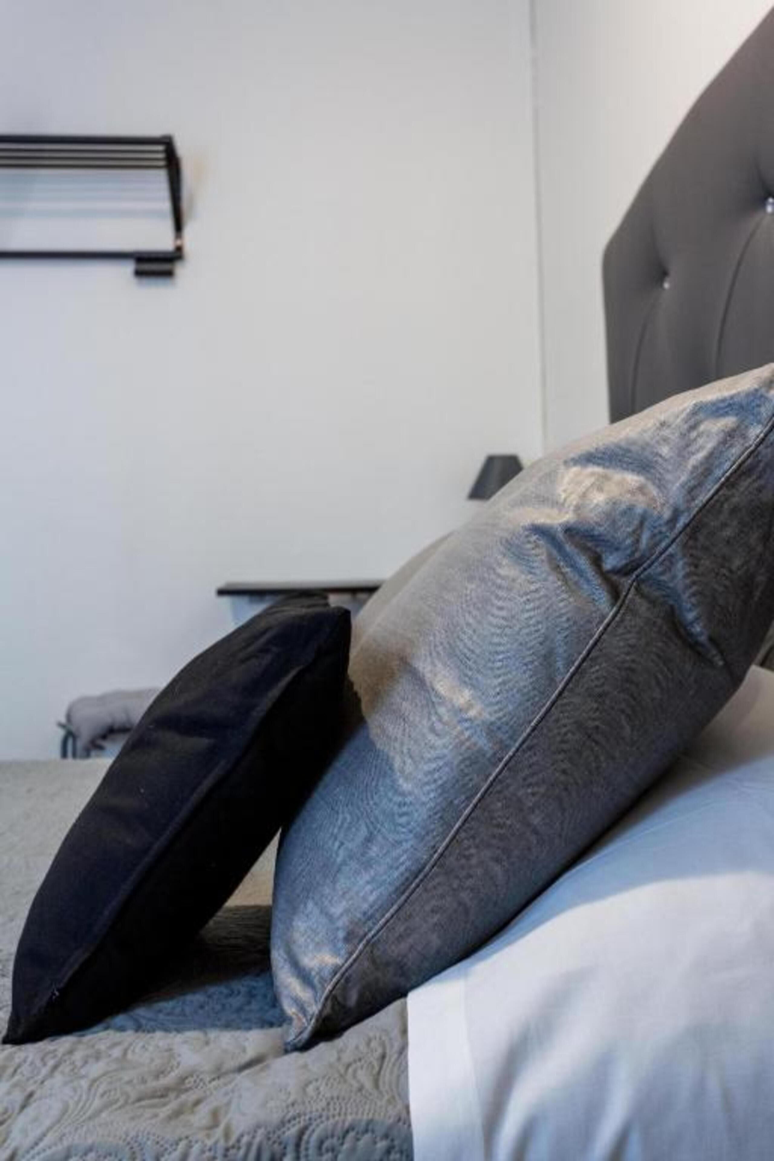 A bed with two pillows, a grey headboard, and a bedside table with a lamp.