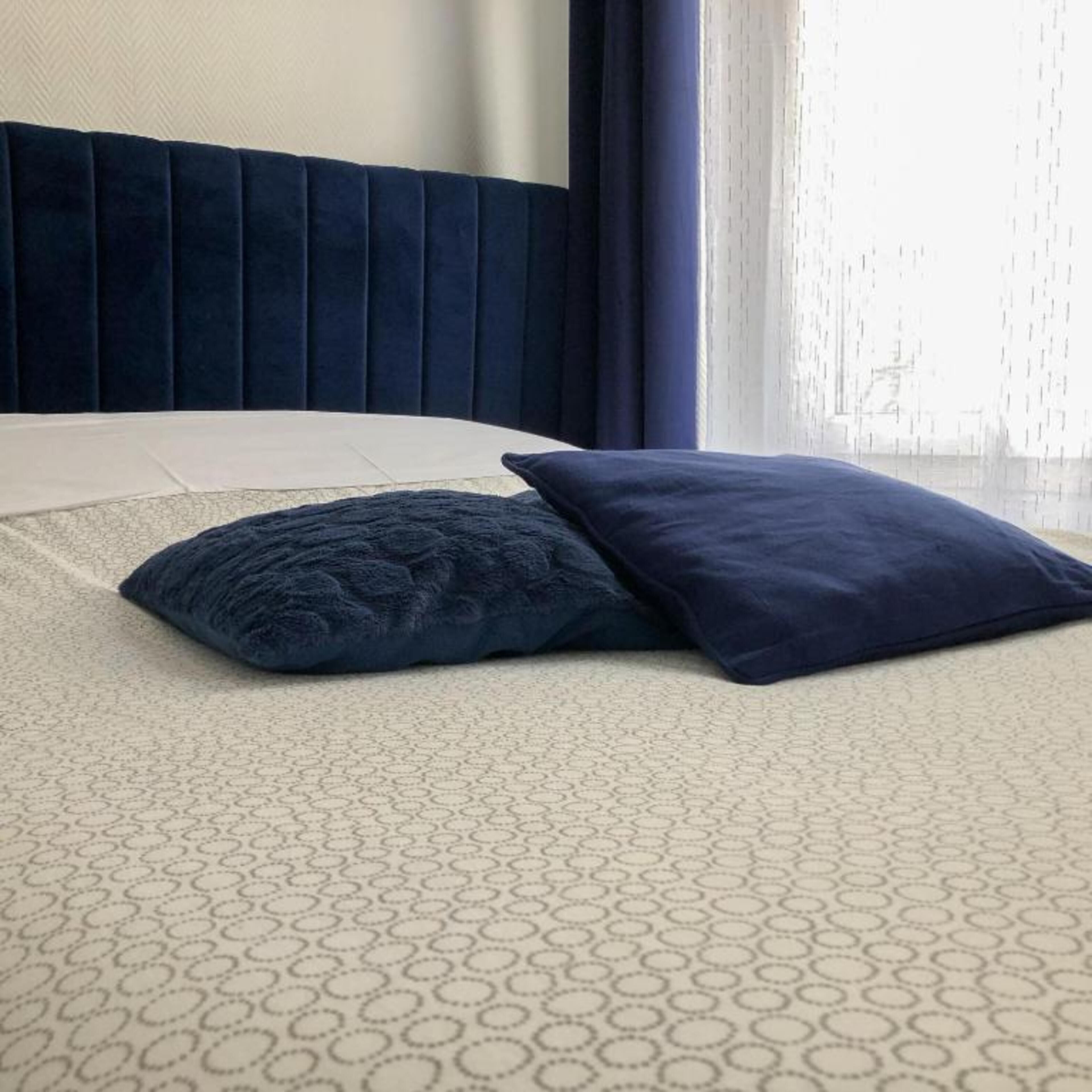 A bed with a patterned bedspread, a dark blue headboard, and two pillows.