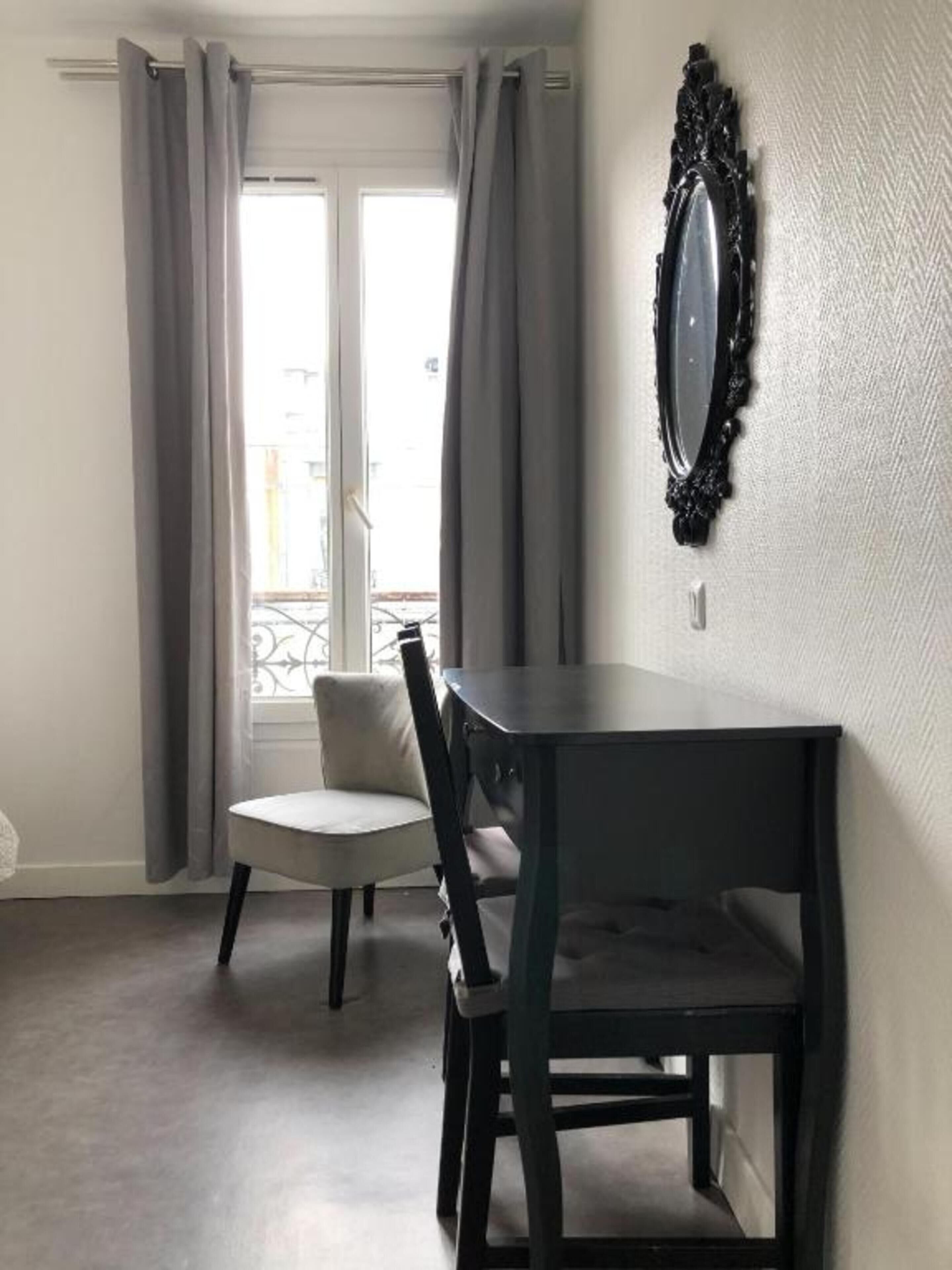 A room with a dining table and chairs, a window with curtains, and a decorative mirror on the wall.