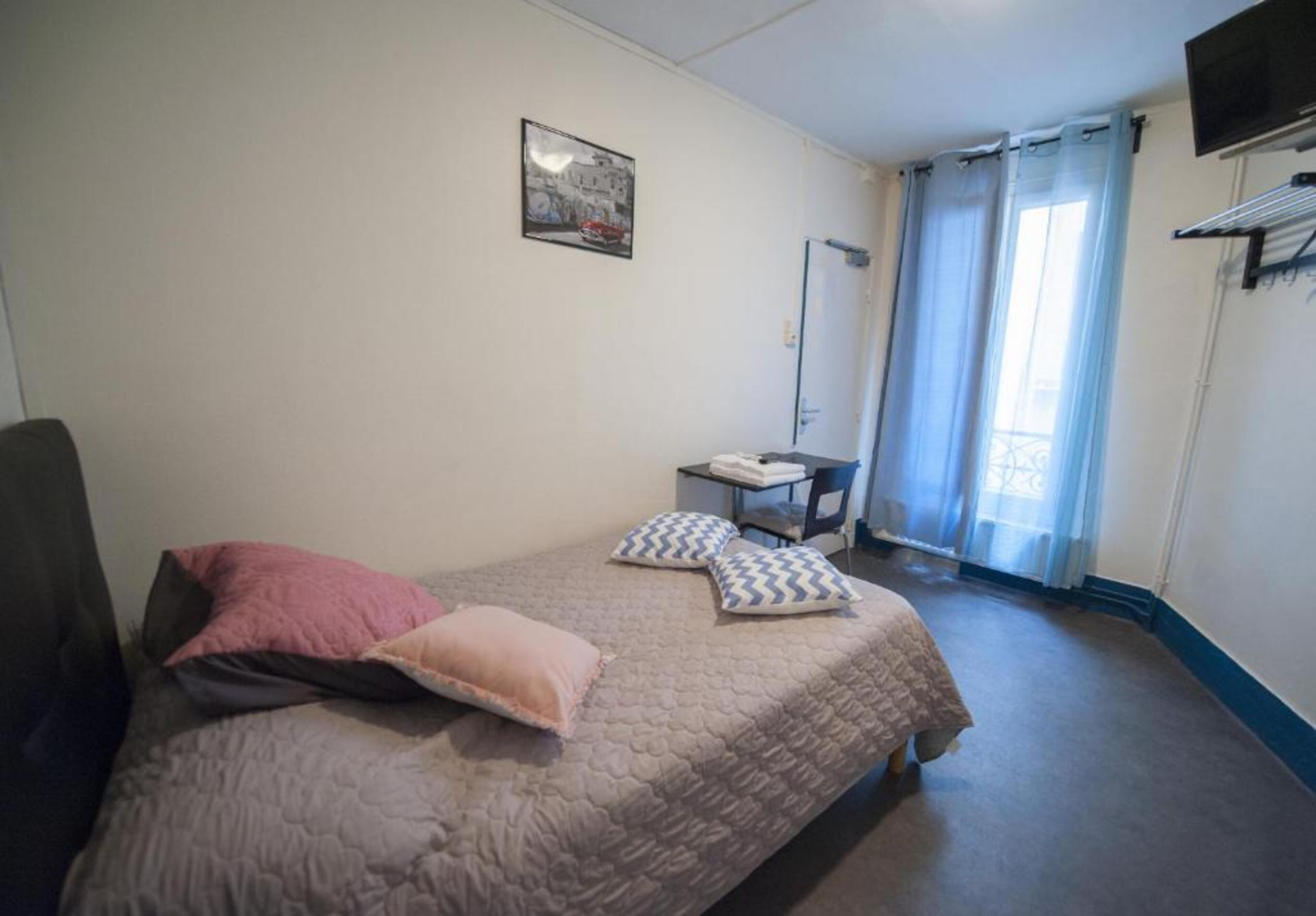 A bedroom with a bed, pillows, a chair, a small table, a TV, and a window with curtains.