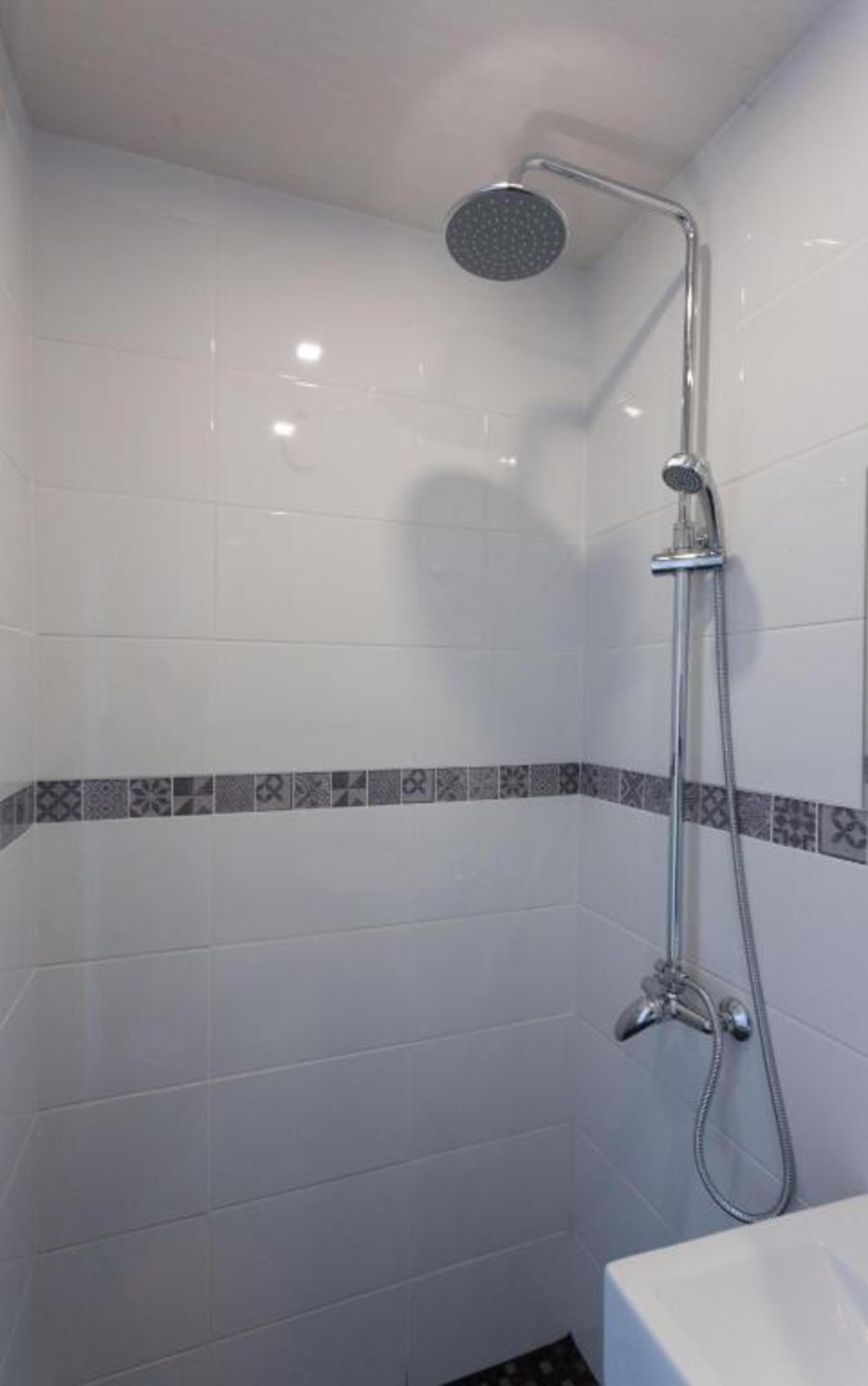 A bathroom with white tiled walls, a shower with a handheld showerhead, and a tiled floor.