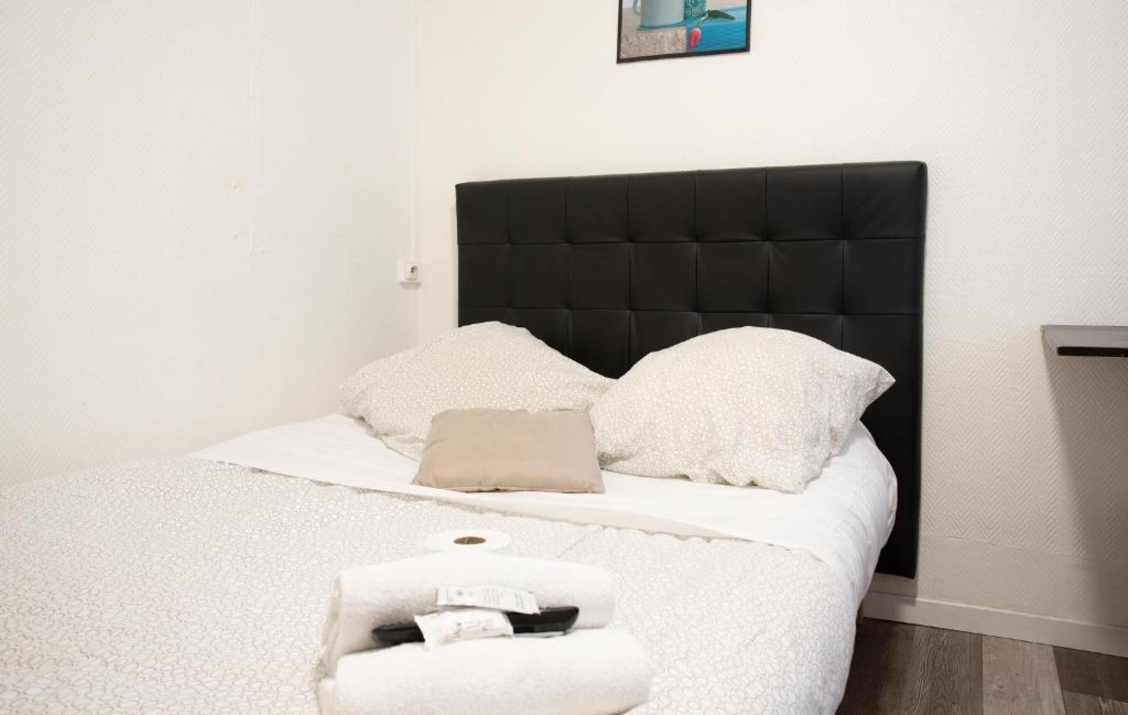 A neatly made bed with a black headboard, white bedding, and a single beige pillow.