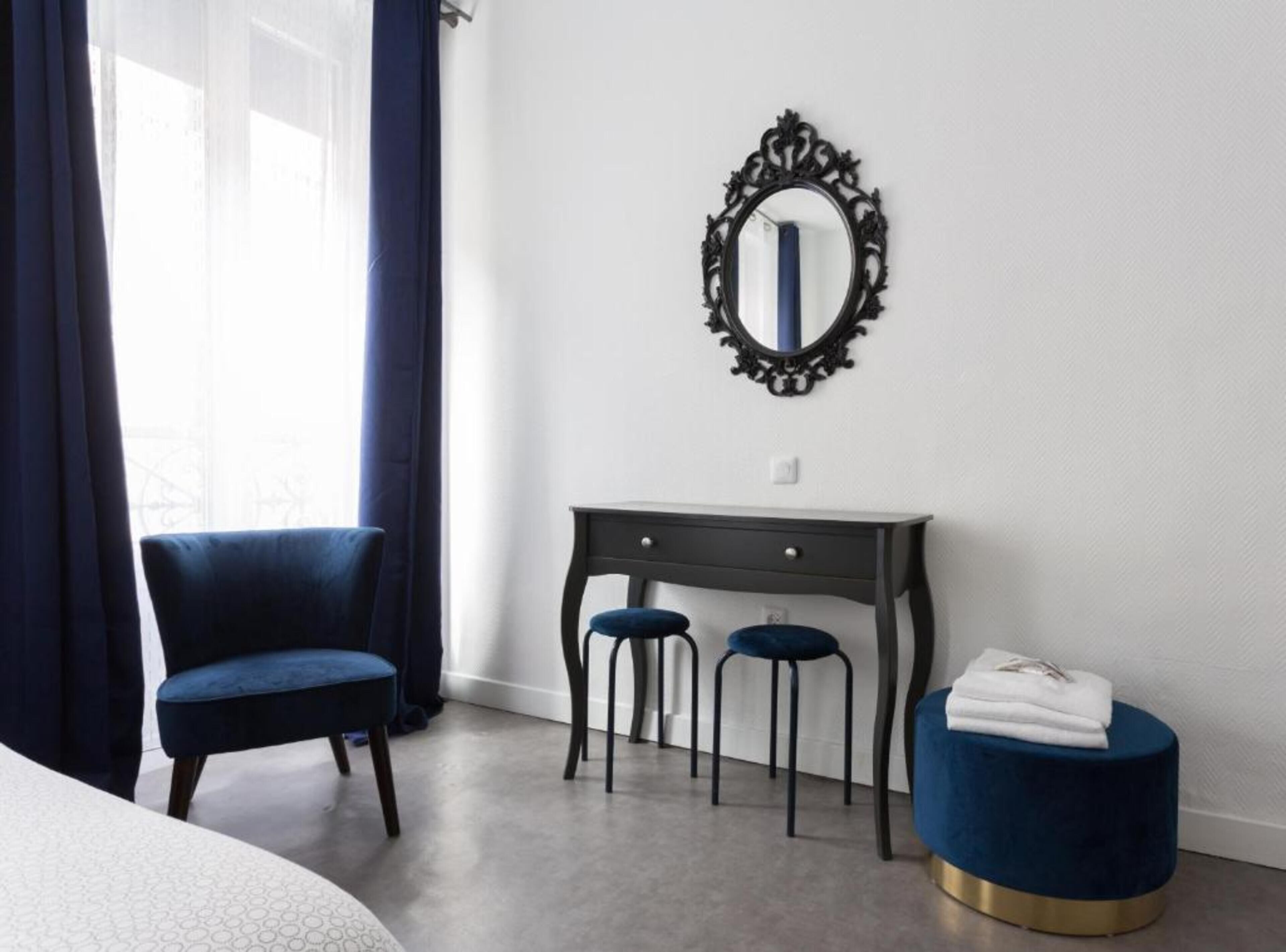 Ein Schlafzimmer mit einem Bett, einem Schreibtisch, zwei Stühlen, einem runden Hocker und einem Spiegel an der Wand.