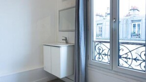 A room with a large window, a white cabinet with a mirror, and a grey curtain. - Europe BLV (Paris)