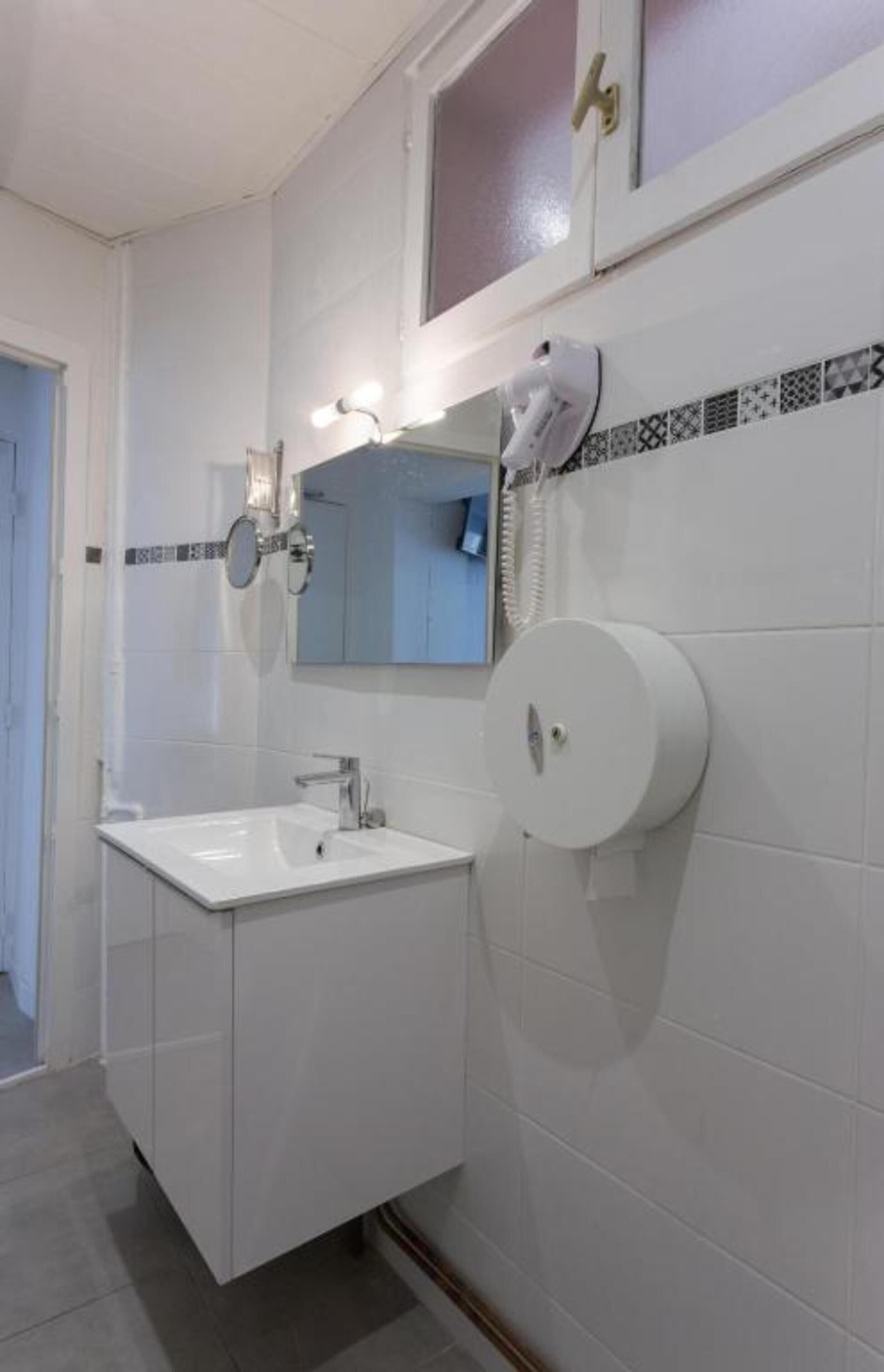Ein Badezimmer mit weißem Waschbecken, einem Spiegel, einem Handtuchspender und einer Toilette.