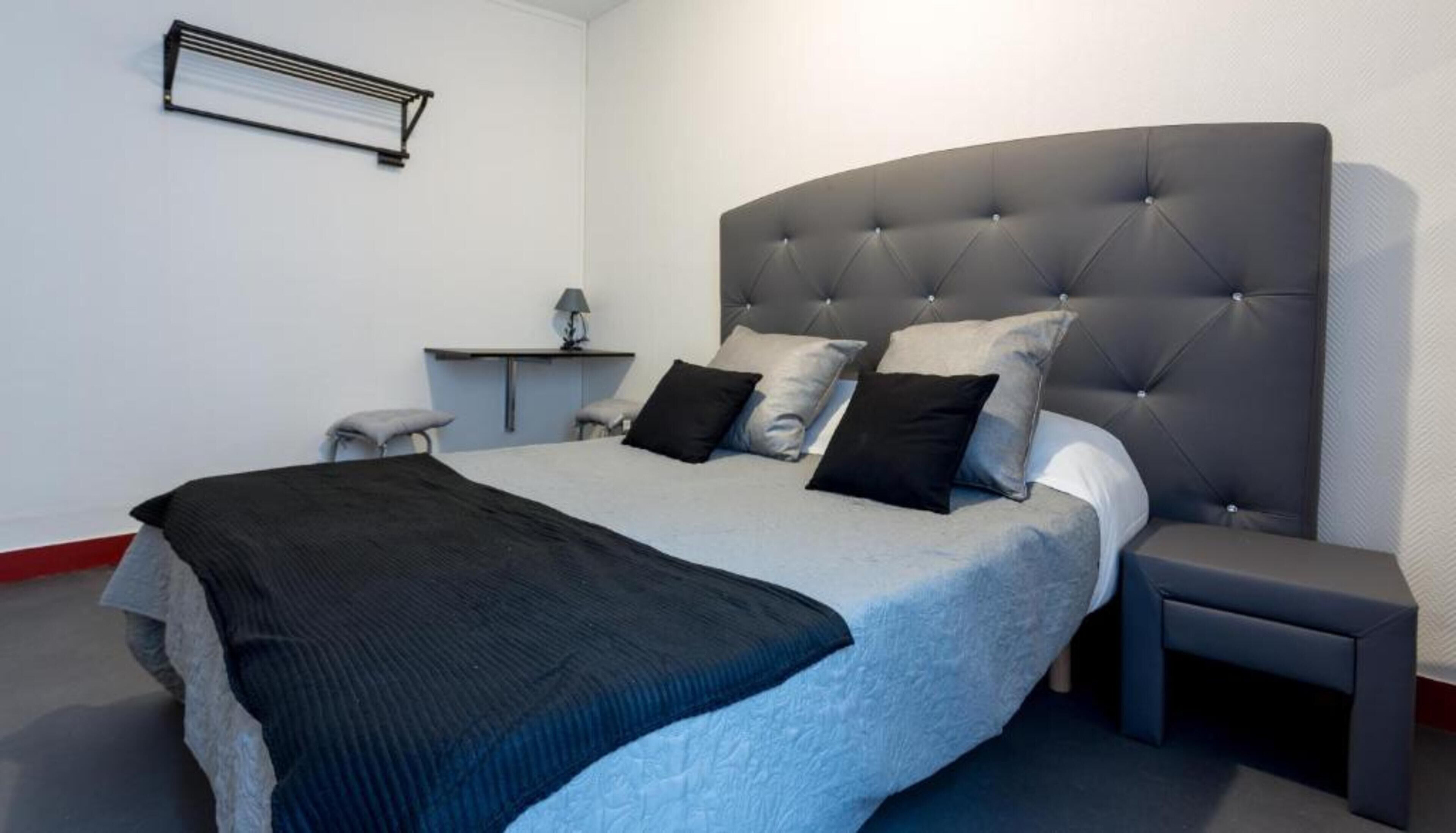 Un dormitorio moderno con una cama grande, una mesita de noche, un escritorio pequeño y un equipo de aire acondicionado instalado en la pared.