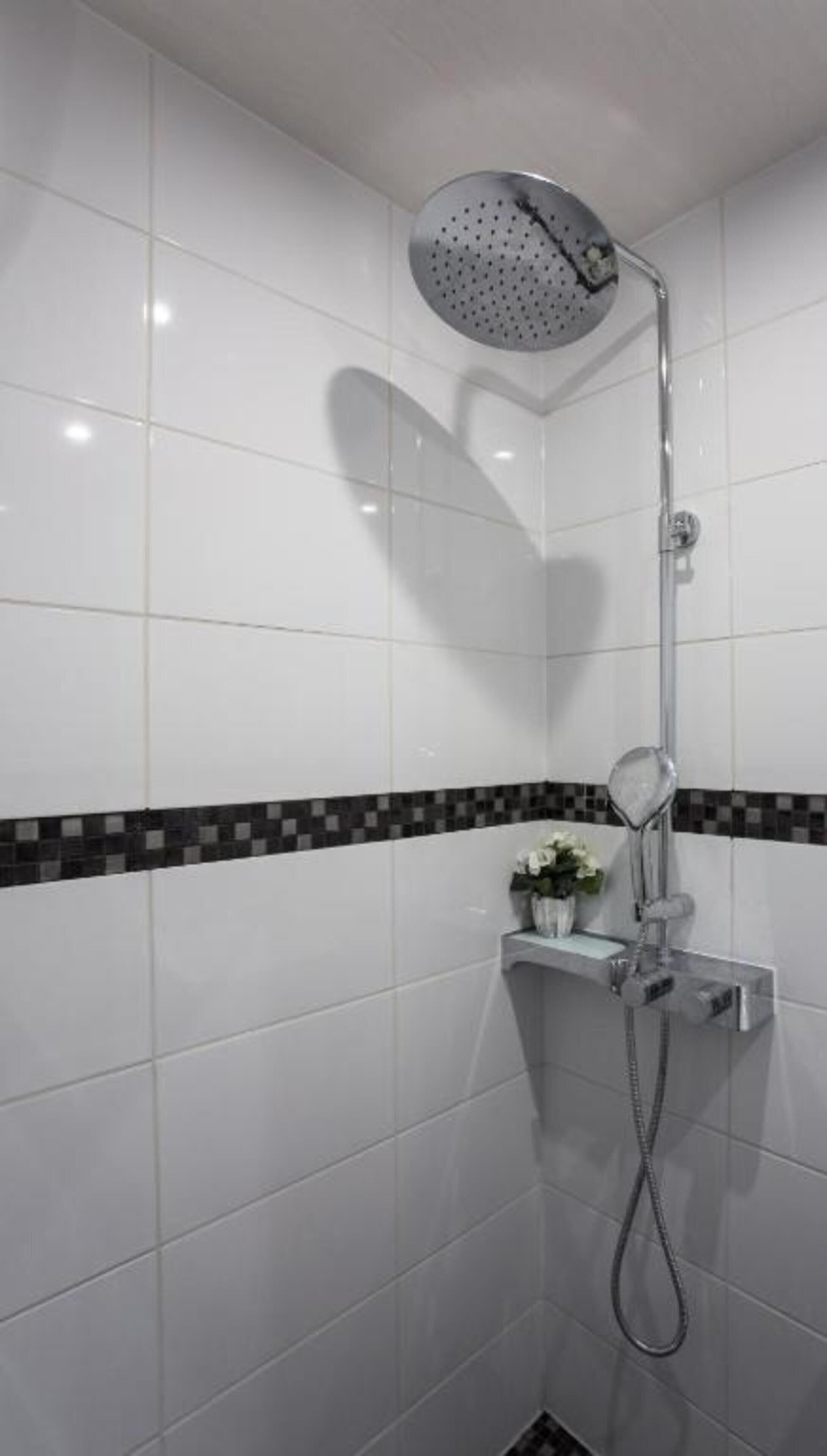 Um chuveiro com a sombra em formato de coração na parede, um pequeno armário com uma planta e piso revestido de azulejos.