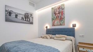 A bedroom with a bed, a blue blanket, a headboard, a nightstand, and two wall-mounted lights. - Apartment 'Casa Parque Benavente' with Private Terrace, Wi-Fi and Air Conditioning (Conil de la Frontera)