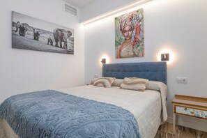 Ein Schlafzimmer mit einem Bett, einer blauen Decke, einem Kopfteil, einem Nachttisch und zwei Wandleuchten.