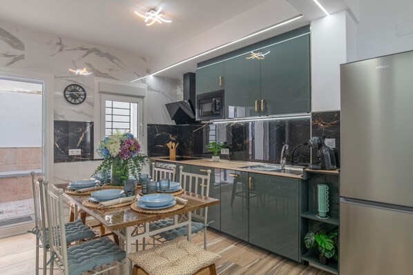 A modern kitchen with a dining area, featuring a built-in microwave, a refrigerator, and a dining table set with plates and a vase of flowers.