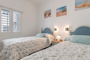 A bedroom with two beds, a window with blinds, and wall-mounted artwork.