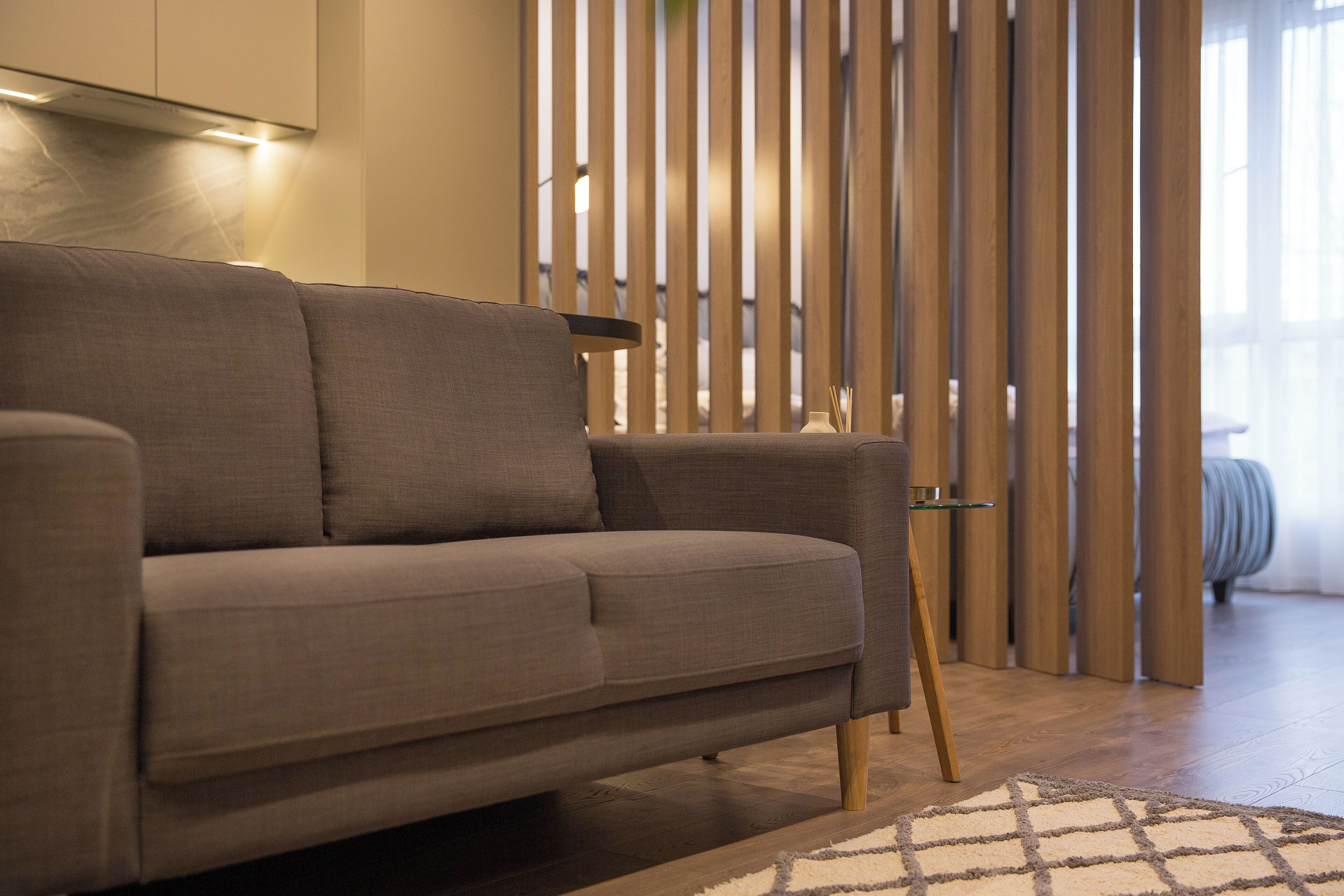Una sala moderna con un sofá gris, listones de madera y una mesa de vidrio.