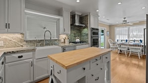 Una cocina moderna con armarios blancos, una isla de madera y un comedor con sillas blancas.