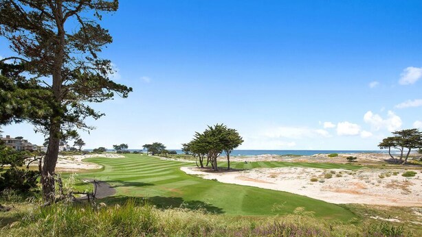 Un campo de golf con bunkers de arena, un obstáculo acuático y un cielo despejado.