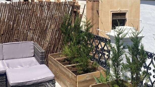 Une terrasse sur le toit agrémentée de jardinières en bois, d’une clôture en fer forgé et d’un bâtiment aux détails architecturaux raffinés.