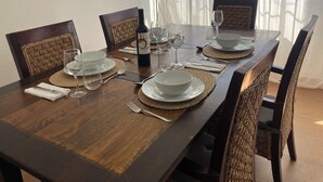 Une table à manger dressée pour quatre personnes, avec des sets de table, des verres à vin et une bouteille de vin.