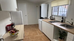 Une cuisine compacte avec des meubles blancs, un plan de travail, un évier, une fenêtre donnant sur un beau paysage et une plante en pot.