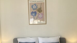 Un lit bien fait, avec deux oreillers, un tableau encadré représentant des fleurs et deux lampes de chevet.