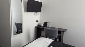 A hotel room with a bed, a desk with a chair, a flat-screen TV mounted on the wall, and a mirror. - OYO Firs Lodge London Heathrow| Standard Single (Hounslow)