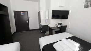 Habitación de hotel con dos camas, un escritorio con computadora, un televisor y un baño con espejo y lavamanos.