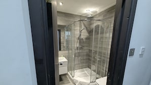 Un baño moderno con ducha envuelta en vidrio, un lavabo blanco y un inodoro.