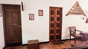 Une porte en bois, un tableau encadré, un meuble en bois et une chaise dans une pièce dont le sol est recouvert de carreaux.