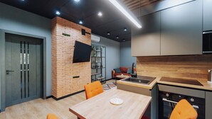 Une cuisine moderne avec un mur d’accent en briques, un coin repas avec des chaises orange et des appareils électroménagers intégrés.