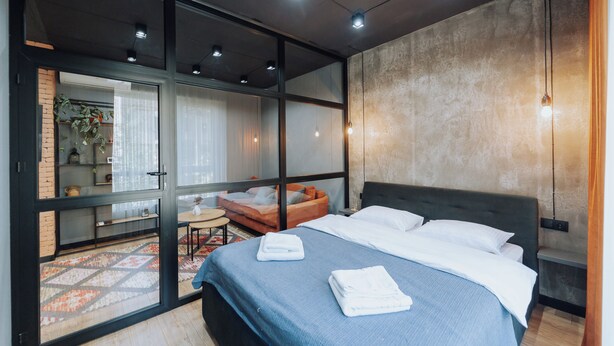 Une chambre moderne avec un grand lit, un canapé et une porte vitrée donnant sur un balcon.