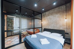 A modern bedroom with a large bed, a sofa, and a glass door leading to a balcony.