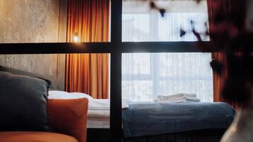 A hotel room with a bed, a window with curtains, and a view of the outside.