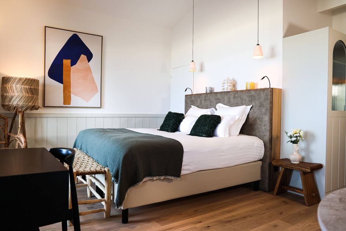 Un dormitorio moderno con una cama grande, una mesita de noche, una silla y una lámpara colgante.