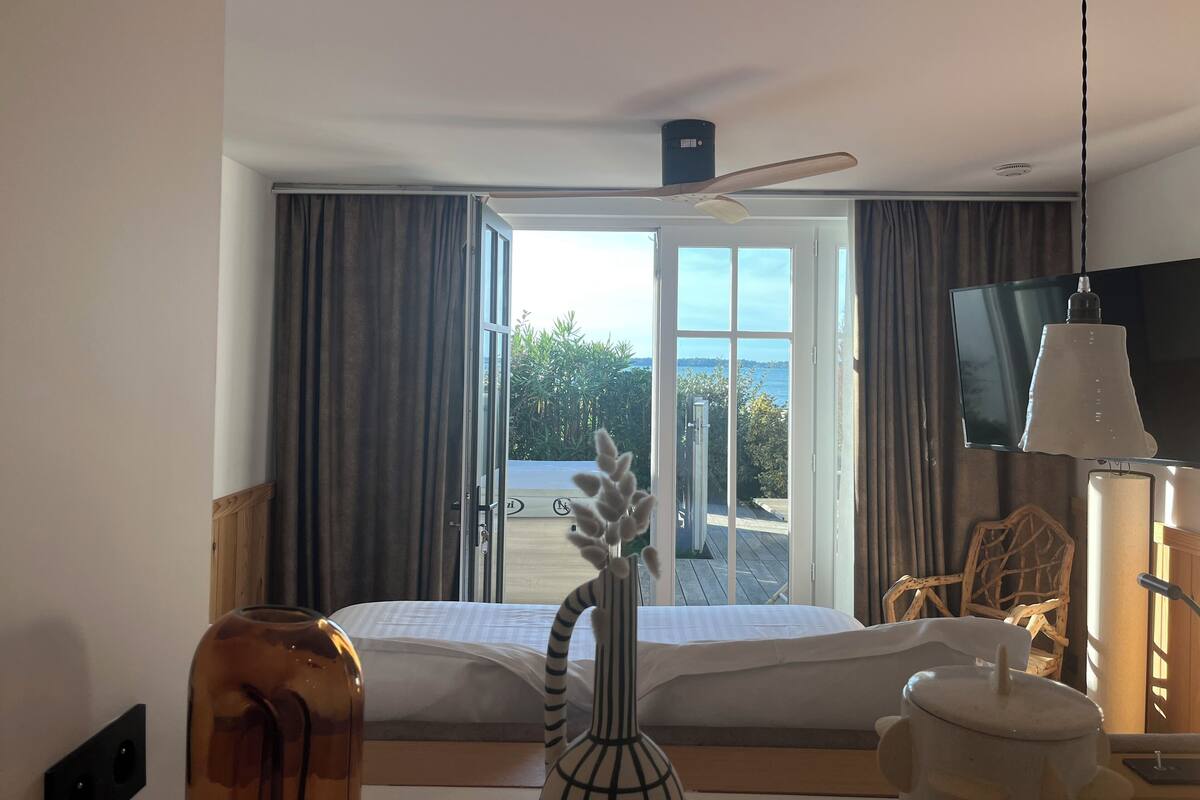 Habitación de hotel con cama, televisión, ventilador de techo y vistas al exterior.