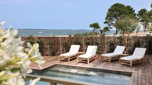 Un espace aménagé au bord de la piscine, avec des chaises longues en bois et une vue sur la mer.