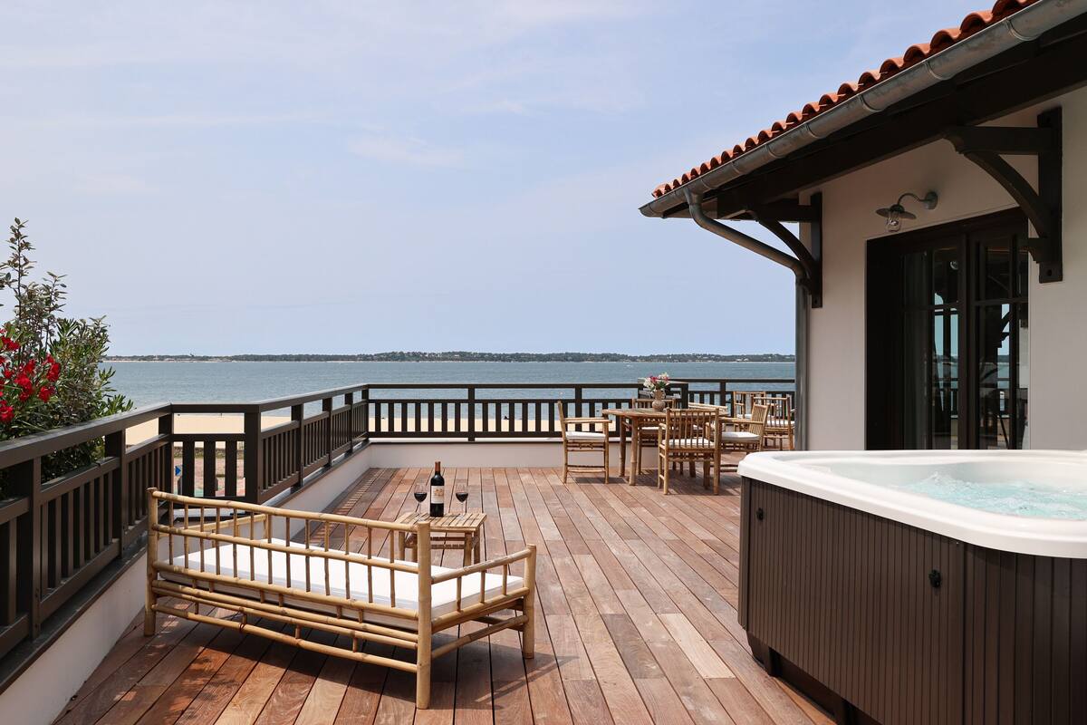 Una terraza de madera con jacuzzi, zona de estar y vistas al mar.