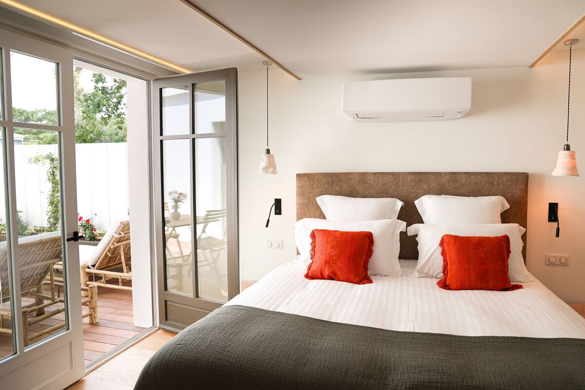 Un dormitorio con una cama grande, dos almohadas, una mesita de noche y un ventanal corredero que da a un área exterior.