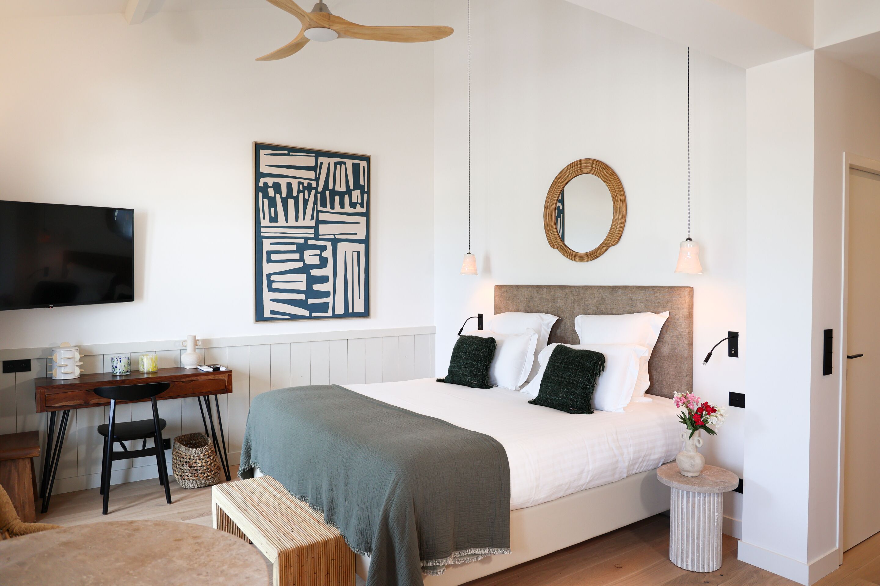 A bedroom with a bed, a desk, a chair, a TV, and a wall-mounted mirror.