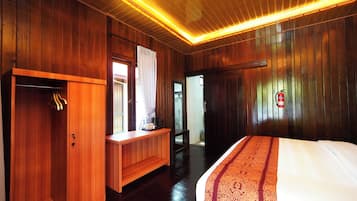 Habitación de hotel con paredes de madera, una cama con colcha estampada, un armario de madera, un escritorio con cafetera y un extintor en la pared.