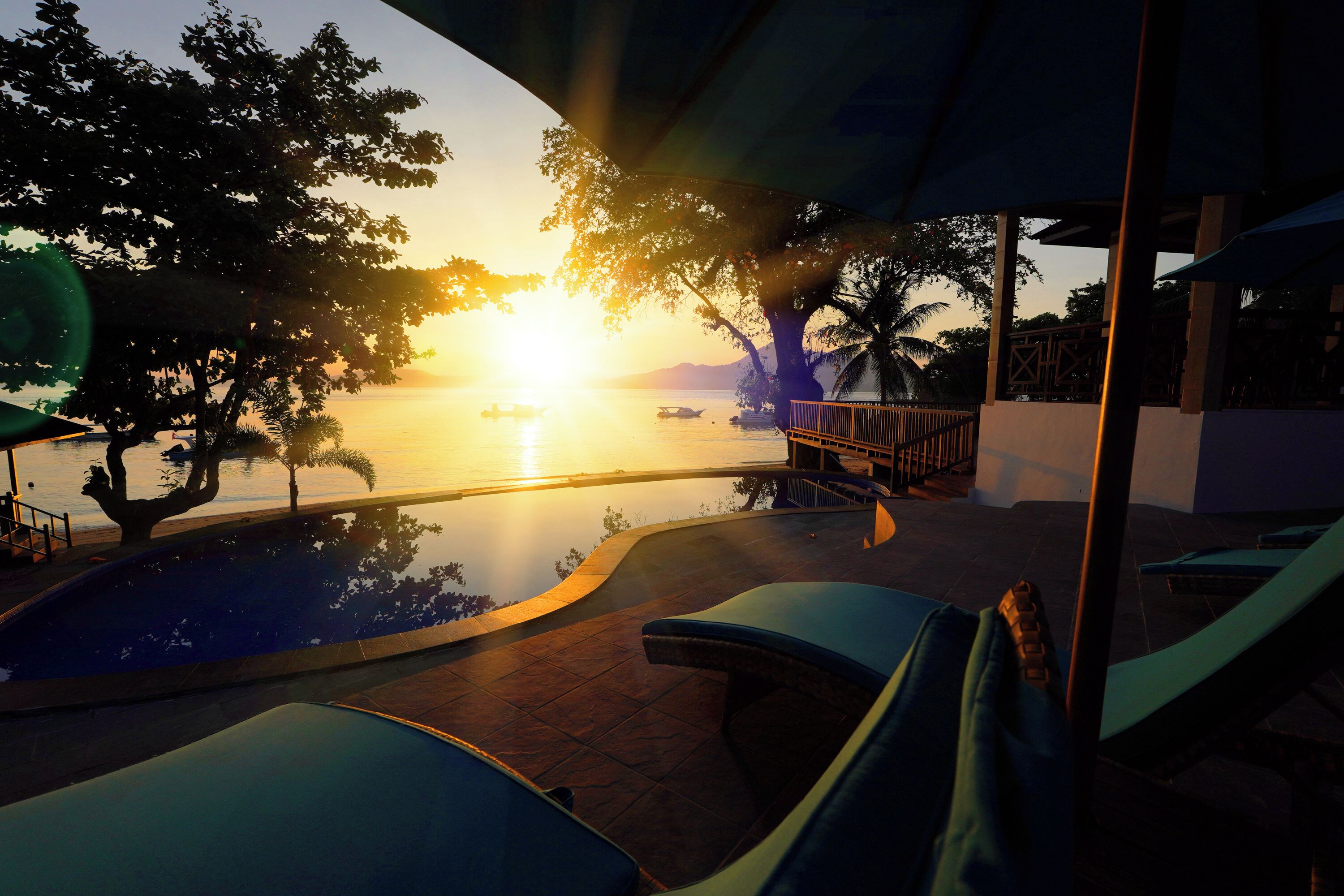 Vista de la piscina con sillones, una alberca y un atardecer sobre el agua.