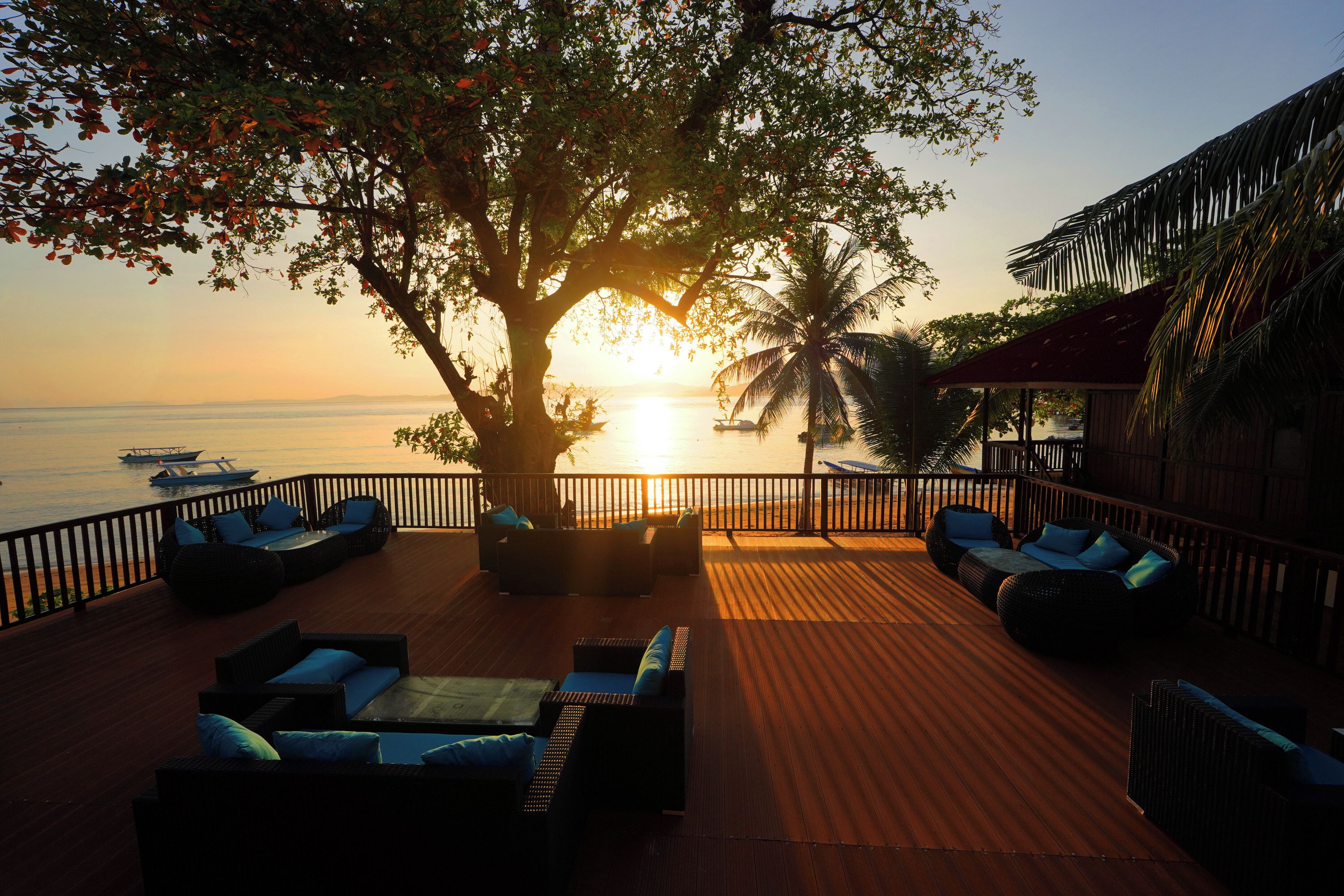 Una terraza con asientos al aire libre, vista al mar y un atardecer.
