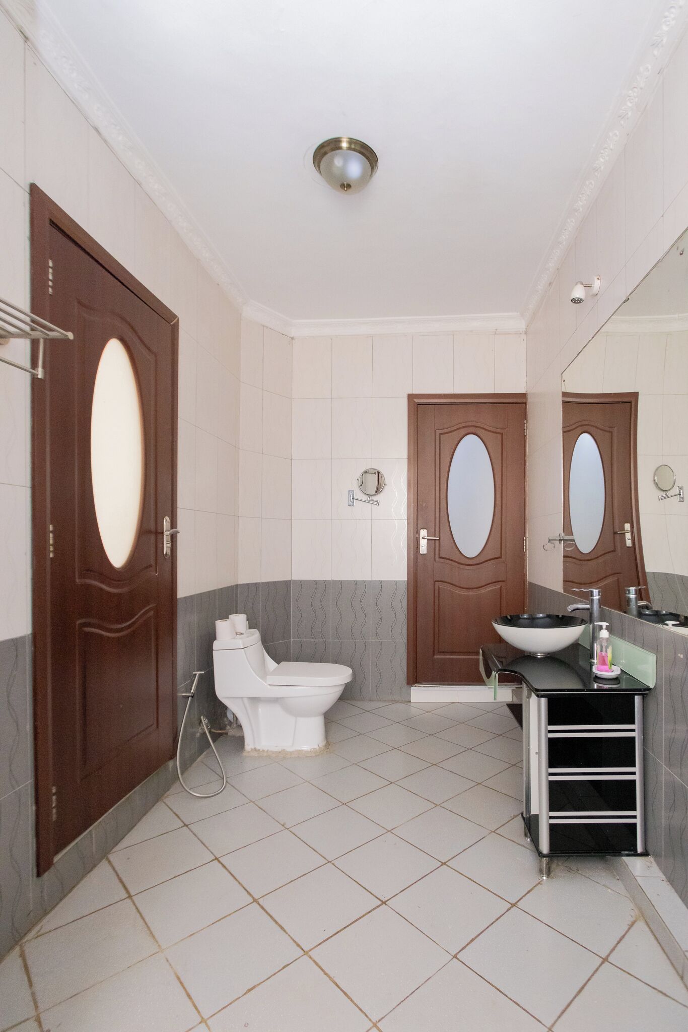 A bathroom with two doors, a toilet, a sink with a mirror, and a shower area.