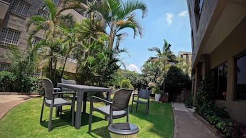 Un área exterior bien cuidada con una mesa y sillas, rodeada de exuberante vegetación y palmeras.
