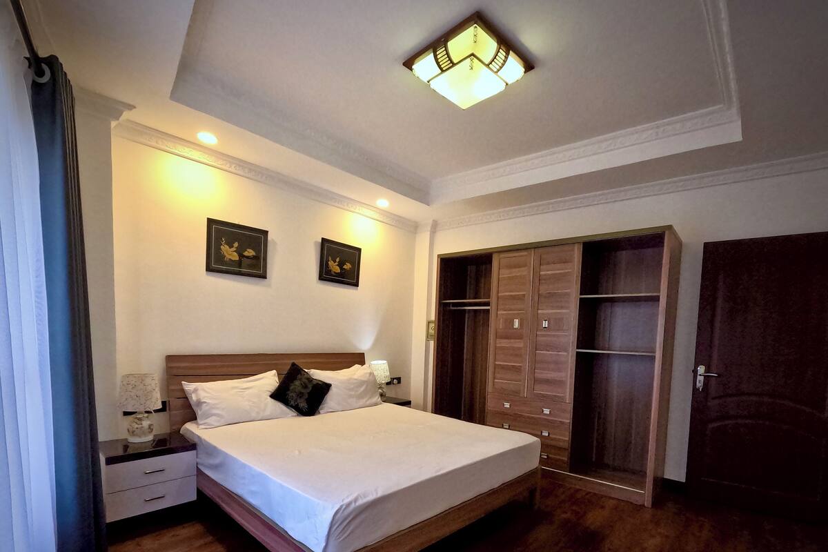 Un dormitorio con cama, mesitas de noche, armario y una lámpara en el techo.