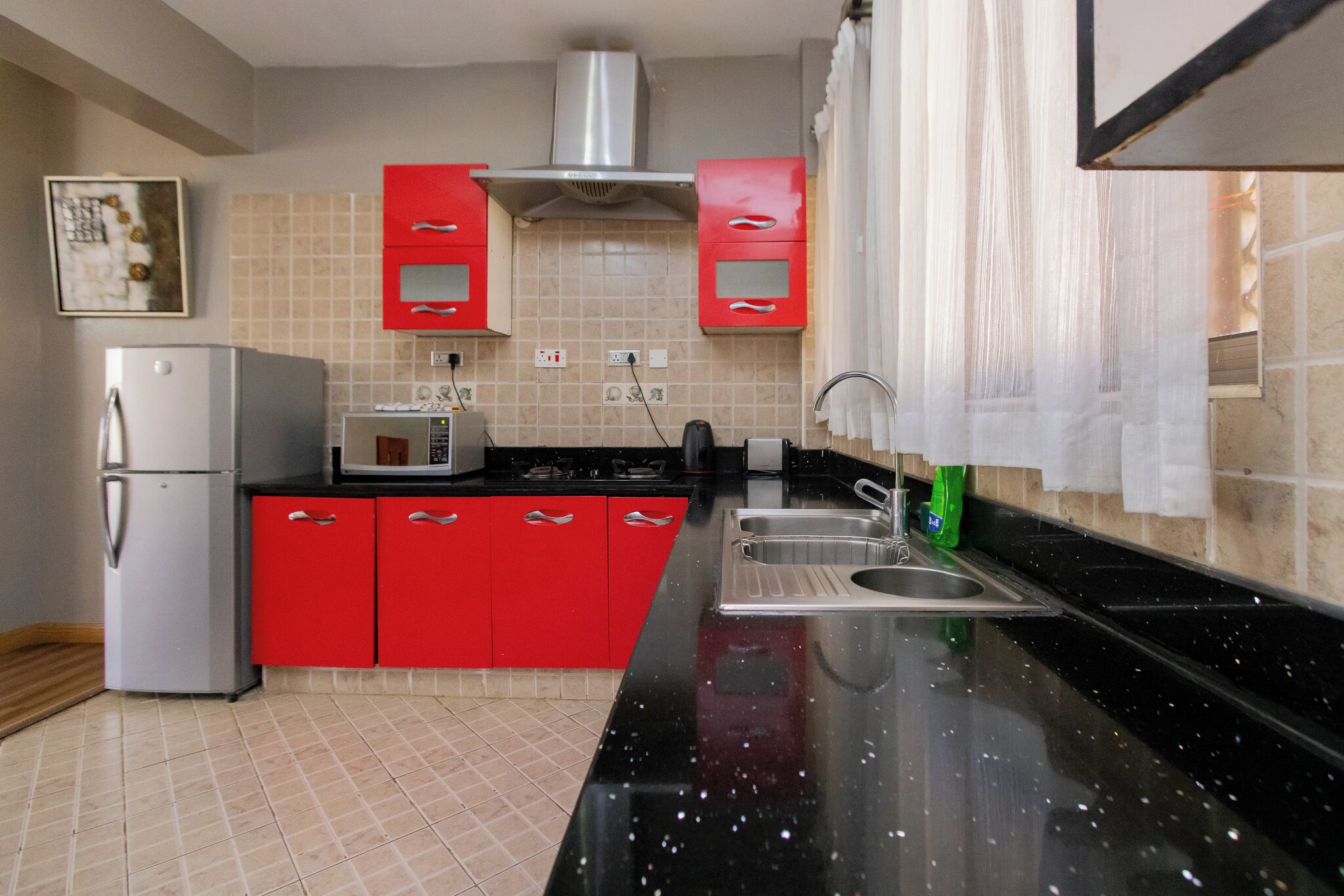 A kitchen with red cabinets, a black countertop, a stainless steel sink, and a microwave.