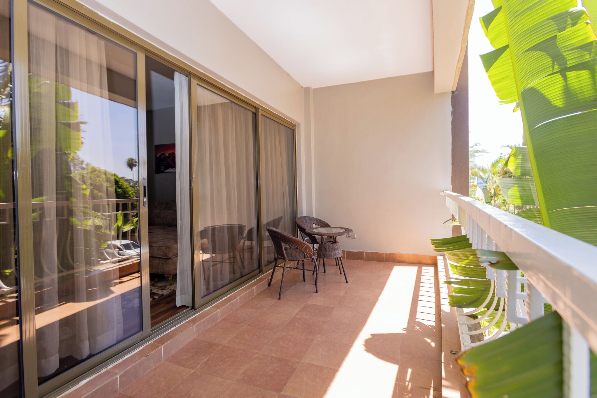 A balcony with a sliding glass door, a small table with chairs, and a railing with green leaves.