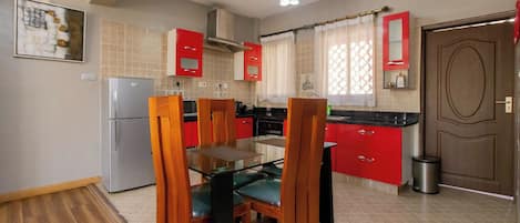 A kitchen with wooden chairs, a glass table, red cabinets, and a stainless steel refrigerator.